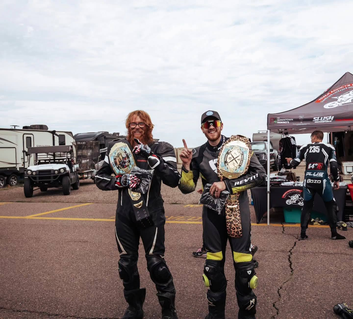 Golden Performance team celebrating back-to-back Festival of Speed Suit Wars championships with winner belts at the track